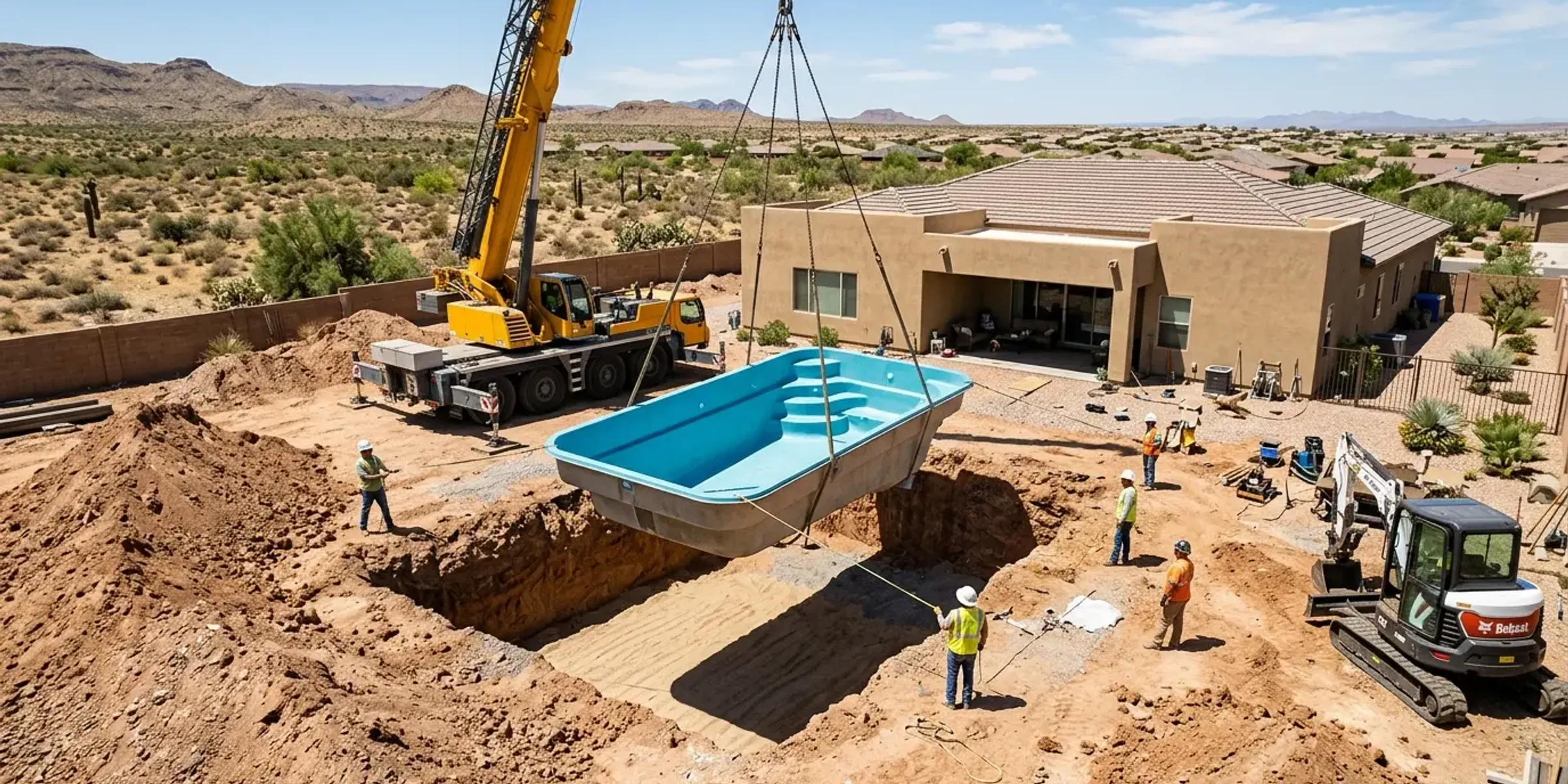 A crew in high-visibility vests lowering a pool shell into an excavated site with a crane and an excavator